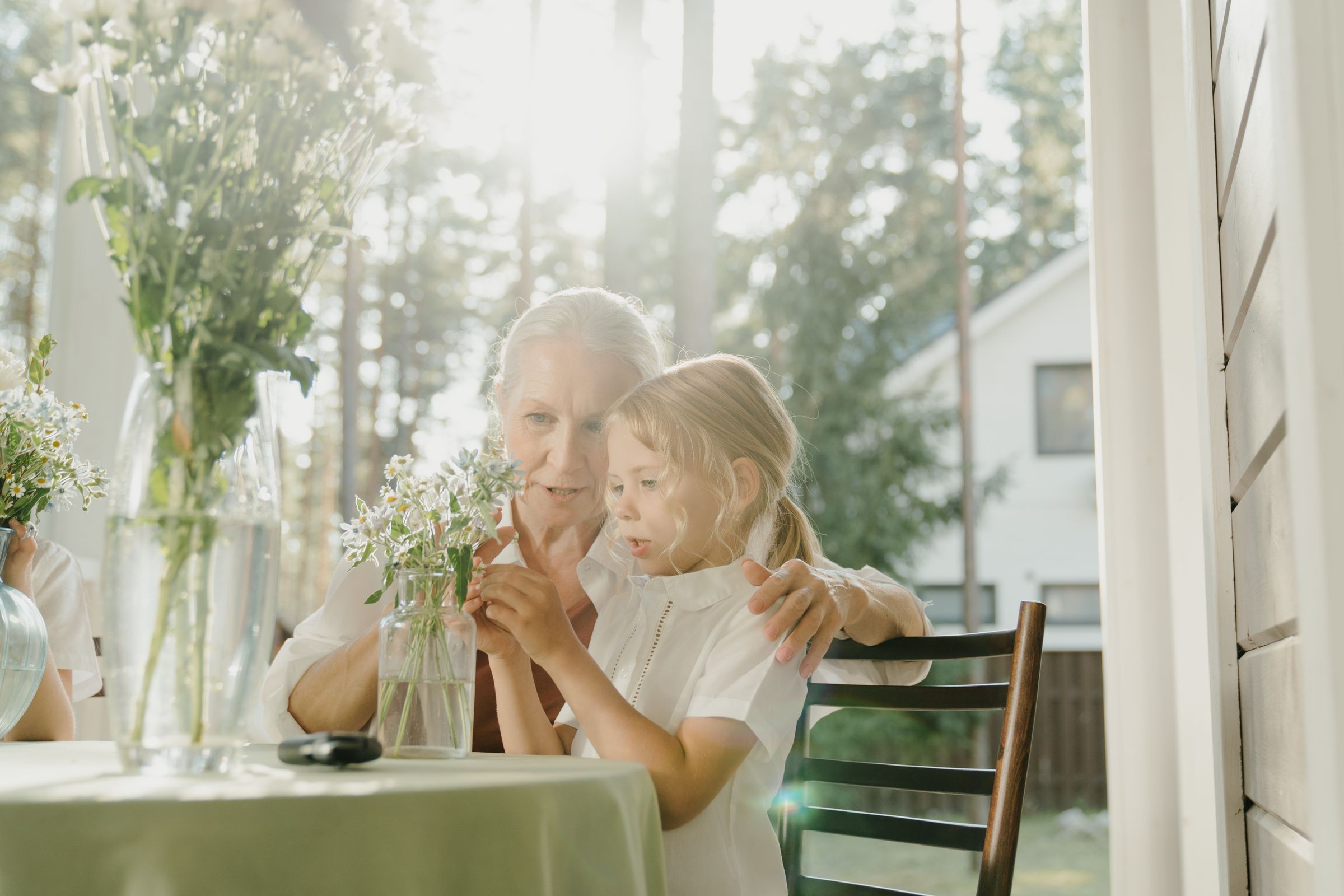 A grandmother and her granddaughter arranging flowers at a table by a sunny window.
